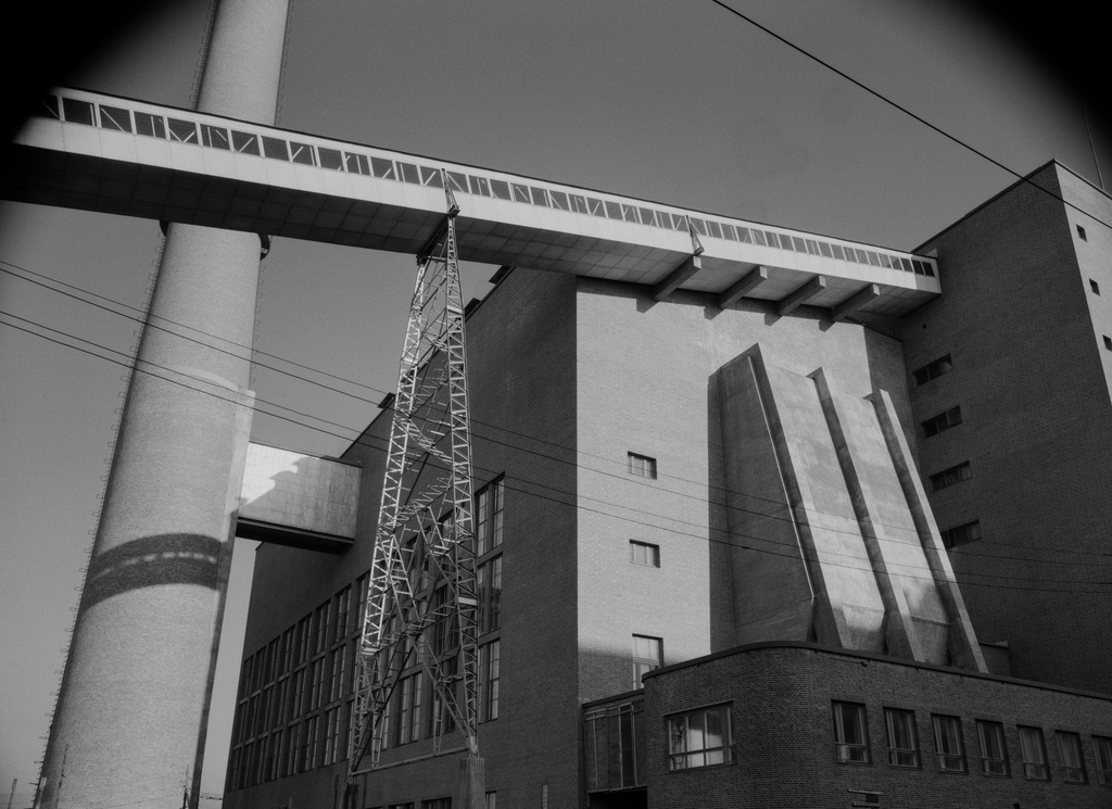 Osa Helsingin sähkölaitoksen Salmisaaren voimalaa, Lauttasaarenkatu 11 (nyk. Porkkalankatu 9-11), nähtynä Tallberginkadun varrelta, Porkkalankadun pohjoispuolelta. Rakennuksen yläkertaan nousee hiiltä voimalan polttoaineeksi kuljettava linjasto. Voimala A:n suunnitteli arkkitehti Vera Rosendal kaupunginarkkitehti Hilding Ekelundin johdolla, ja se otettiin käyttöön vuonna 1953. Valokuvan ylänurkissa näkyvät kaareutuvat tummat varjot, jotka johtuu siitä, että valokuvaaja on käyttänyt kuvatessaan vastavalosuojaa.