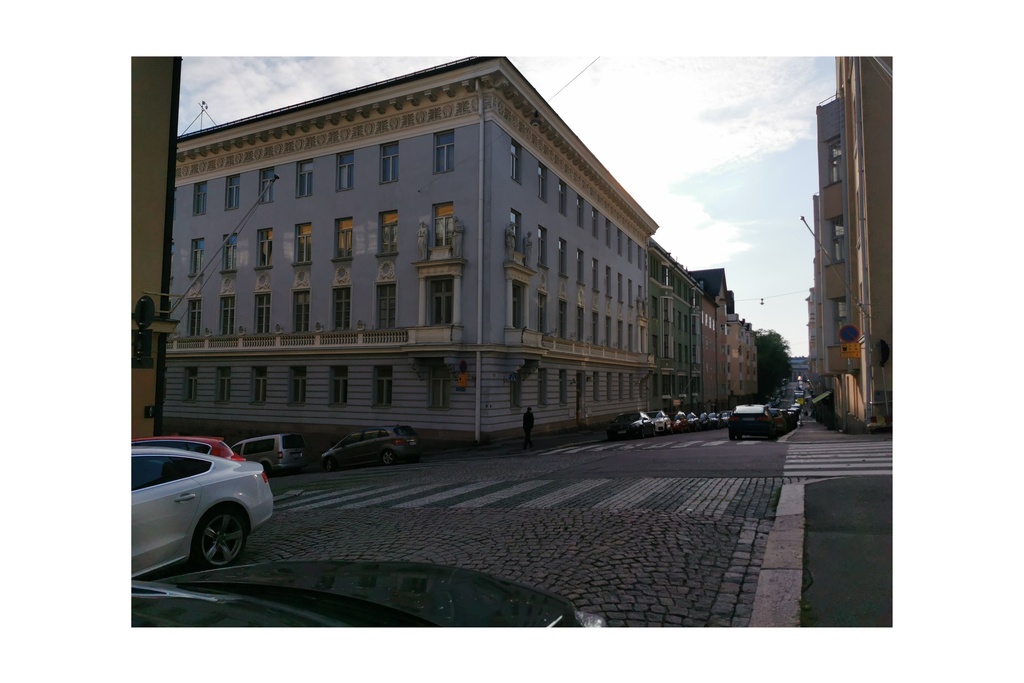 Pysäköityjä autoja ja lunta kadun varressa Rauhankadulla. Näkymä Meritullinkadun kulmasta länteen, Mariankadun suuntaan. Edessa tien toisella puolella näkyy Rauhankatu 4 ja Meritullinkatu 10 kulmaan asettuva patsain koristeltu rakennus. Rakennus on Georg Wasastjernan suunnittelema, 1914 rakennettu ja tyyliltään klassistinen. Talo on ollut opetusministeriön käytössä vuodesta 1968. rephoto