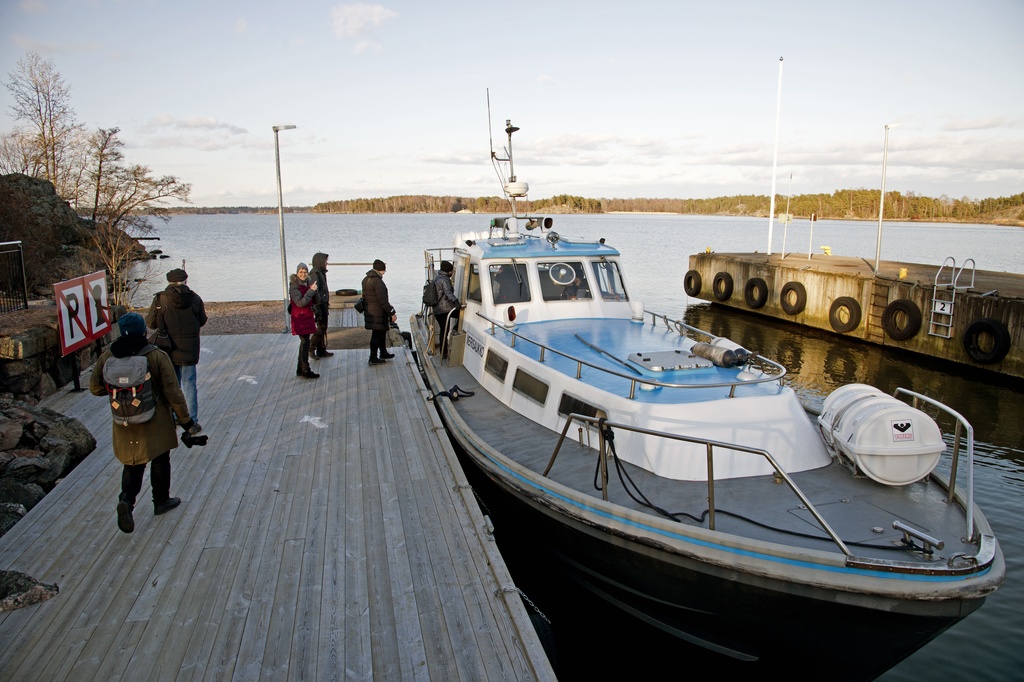Retkeläiset menossa taksiveneeseen Vallisaaressa. Paikka on Torpedolahden laituri Vallisaaren itärannalla. Taivaanrannassa Haminansalmen toisella puolen näkyy Santahamina.
