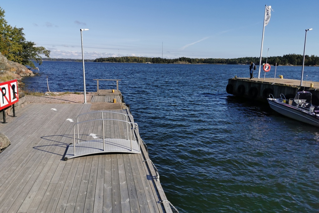 Retkeläiset menossa taksiveneeseen Vallisaaressa. Paikka on Torpedolahden laituri Vallisaaren itärannalla. Taivaanrannassa Haminansalmen toisella puolen näkyy Santahamina. rephoto