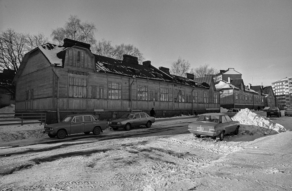 Näkymä pitkin Kirstinkujaa kohti Porvoonkatua, Kirstinkuja 4, 6, Vesilinnankatu 17 sekä äärimmäisenä oikealla Porvoonkatu 19. Kadun varrelle on pysäköity henkilöautoja ja koottu korkea lumikinos.