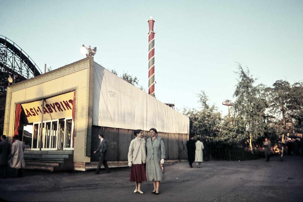 Linnanmäki. Ihmisiä huvipuistossa, keskellä lasi-labyrintti -rakennus. Taustalla vasemmalla vuoristorata.