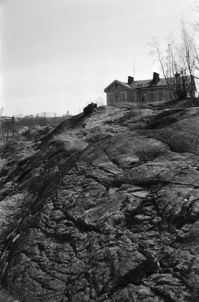 Linnunlauluntie. Kaksi poikaa (Aapo Rista ja Tuomas Heikkilä) tutkimassa keväistä luontoa Linnunlaulun kallioilla radan varressa. Näkymä radan ylittävän sillan kupeesta kaakkoon. Oikealla kallion laella Linnunlauluntie 12:n talo.