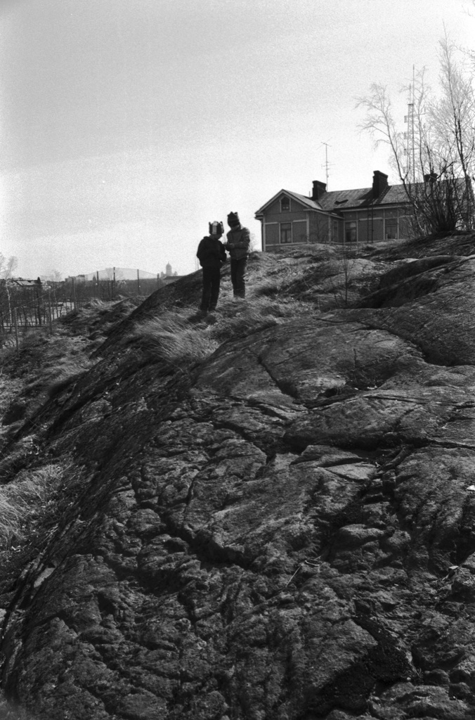 Linnunlauluntie. Kaksi poikaa (Aapo Rista ja Tuomas Heikkilä) tutkimassa keväistä luontoa Linnunlaulun kallioilla radan varressa. Näkymä radan ylittävän sillan kupeesta kaakkoon. Oikealla kallion laella Linnunlauluntie 12:n talo.