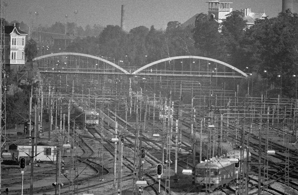 Näkymä Helsingin päärautatieaseman rakennuksen kellotornista pohjoiseen. Maisema avautuu ratapihan yli. Maiseman poikki menee Linnunlaulun silta ja sen vasemmassa päässä näkyy huvila Linnunlauluntie 15. Ratapihan toisella puolen näkyy toinen vaalea puuhuvila. Etualalla kulkee sähköjunia.