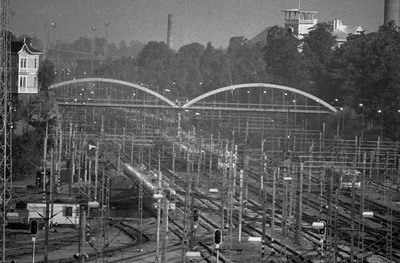 Näkymä Helsingin päärautatieaseman rakennuksen kellotornista pohjoiseen. Maisema avautuu ratapihan yli. Maiseman poikki menee Linnunlaulun silta ja sen vasemmassa päässä näkyy huvila Linnunlauluntie 15. Ratapihan toisella puolen näkyy toinen vaalea puuhuvila. Etualalla kulkee sähköjunia.  similar photo