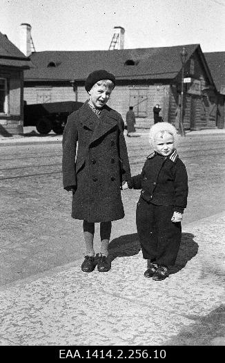 Plastic negative two children standing. Behind low houses and truck.