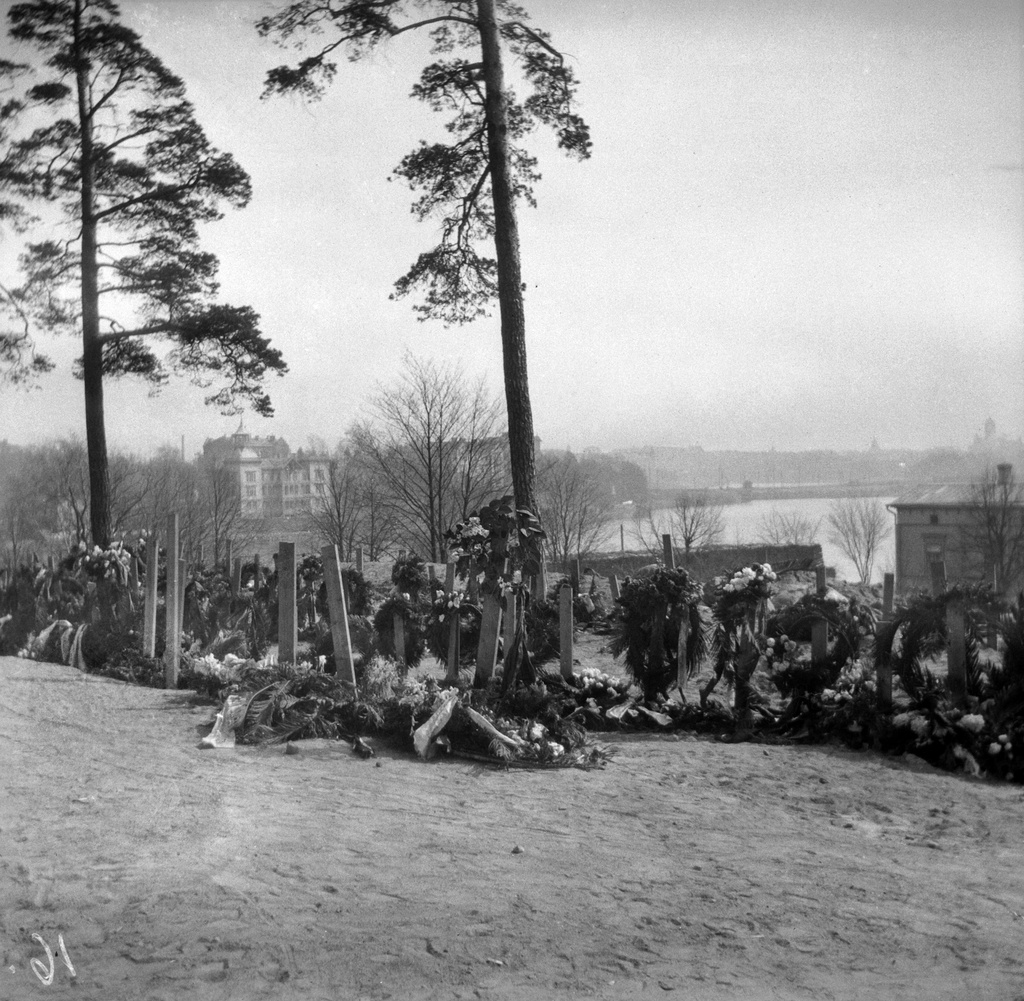 Punakaartilaisten hautoja Mäntymäellä keväällä 1918. Punaiset käyttivät aluetta kaatuneiden sankarihautausmaana. Helsingin valtauksen jälkeen vainajat siirrettiin joukkohautoihin Malmille. Timiriasew kuvasi vuonna 1918 myös sodan toisen osapuolen kaatuneitten hautoja.