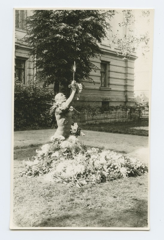 Broken monument layer at the Real School. In the form there are blue white flags, the foot of the pillar is covered with flowers.