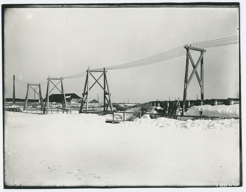 Winter view of some facility - bridge or tamcing, electric line at the forefront, about 1910.