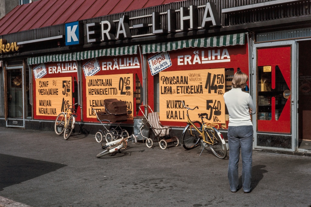 Elintarvikemyymälä Erä-liha, Kettutie 2. K-ketjuun kuuluneen kaupan edessä lastenvaunut ja -rattaat ja polkupyöriä. Kaupan ikkunassa tuotteiden hinnoista kertovia mainoksia.