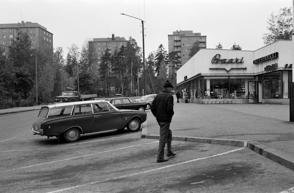 Hiihtäjäntie 1, Herttoniemen ostoskeskus. Taustalla Hiihtäjäntie 2 ja 4. Pysäköityjä henkilöautoja, etualalta taakse laskien: Ford Taunus 17M Turnier, Peugeot 404, Volkswagen, Ford Cortina.