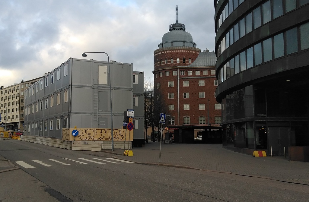 Rakennuksia ja aidattu puutavaran varastointialue nykyisen Ympyrätalon paikalla. Oikealla Porthaninrinne 1 ja 3. Vasemmalla Toinen linja 5 ja Porthaninkatu 1. Taustalla Arena talo. rephoto
