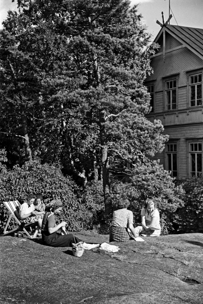 Naisia istumassa ulkona kalliolla ja aurinkotuoleissa Pihlajasaaressa. Oikealla näkyy nk. "Elannon huvila", Wästanhäll.