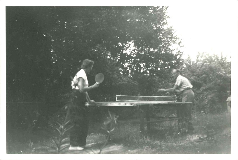 A woman and a man play in table tennis; outdoors in summer