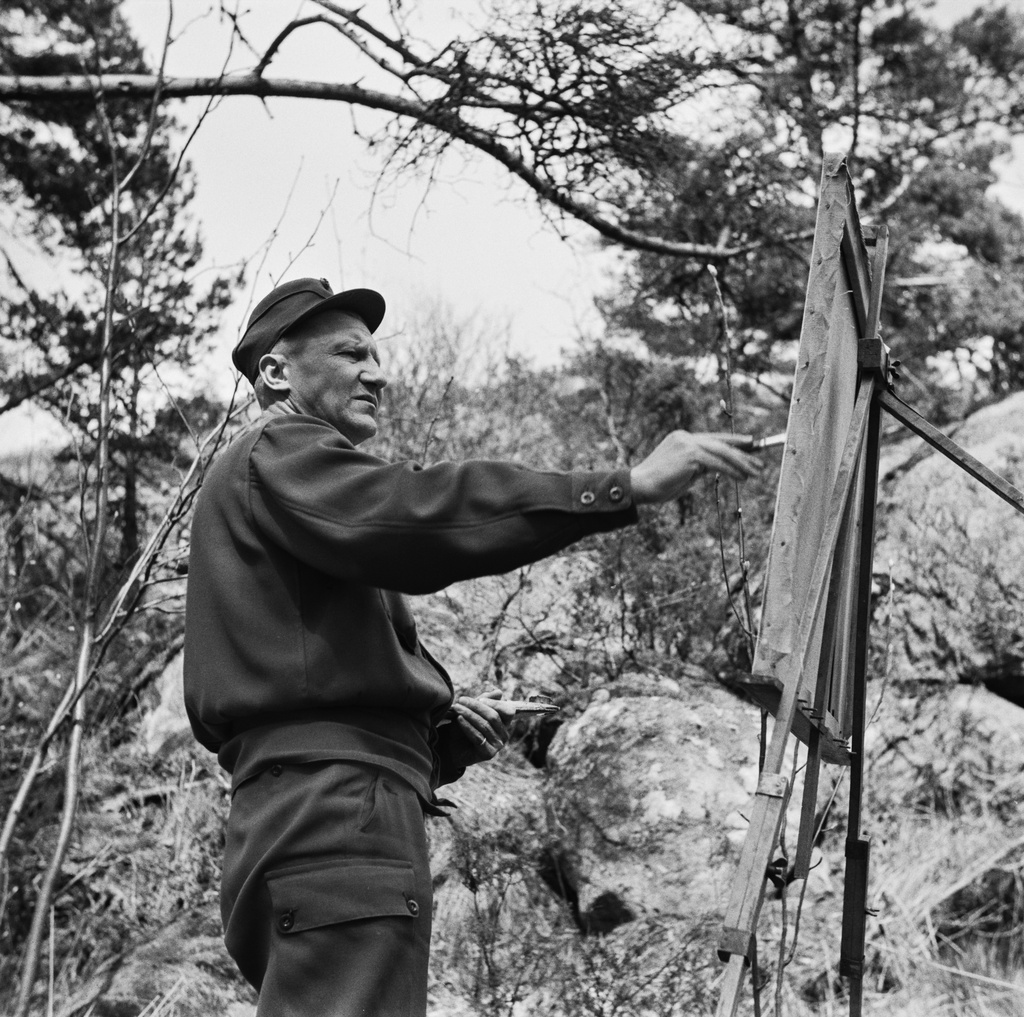 Toivo Kautonen maalaa maisemaa Vallisaaressa. Valokuva on otettu alaviistosta. Maalaajan käsi on liike-epäterävä siveltimen vetojen vaikutuksesta.