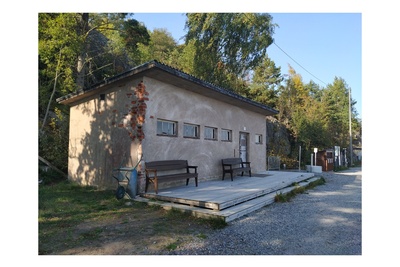 Näkymä Vallisaaren itärantaa kulkevalle tielle. Se on retkisataman tuntumassa jo suurin piirtein Kuninkaansaarta vastapäätä. Punatiilinen rakennus vasemmalla liittyy saaren torpedoluolaston toimintaan. Rakennus on rapattu harmaalla laastilla, josta osa on karissut pois. Rakennuksen päätyä vasten nojaa lavoja ja julkisivun edustalle on rakennettu alusta. Äärimäisenä oikealla pilkottaa meri. rephoto