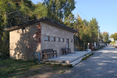 Näkymä Vallisaaren itärantaa kulkevalle tielle. Se on retkisataman tuntumassa jo suurin piirtein Kuninkaansaarta vastapäätä. Punatiilinen rakennus vasemmalla liittyy saaren torpedoluolaston toimintaan. Rakennus on rapattu harmaalla laastilla, josta osa on karissut pois. Rakennuksen päätyä vasten nojaa lavoja ja julkisivun edustalle on rakennettu alusta. Äärimäisenä oikealla pilkottaa meri. rephoto