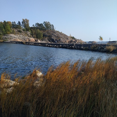 Juhannuskokko Kuninkaansaaren ja Vallisaaren välissä. Kokko on koottu saarten väliin rakennetun vallin päällä kulkevalle tielle. Valokuva on otettu Vallisaaren puolelta siten, että taustalla näkyy Kuninkaansaari. Kokon läheisyyteen on kerääntynyt ihmisiä seuraamaan roihua. rephoto