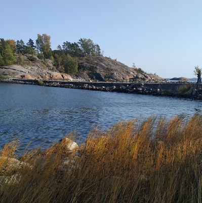 Juhannuskokko Kuninkaansaaren ja Vallisaaren välissä. Kokko on koottu saarten väliin rakennetun vallin päällä kulkevalle tielle. Valokuva on otettu Vallisaaren puolelta siten, että taustalla näkyy Kuninkaansaari. Kokon läheisyyteen on kerääntynyt ihmisiä seuraamaan roihua. rephoto