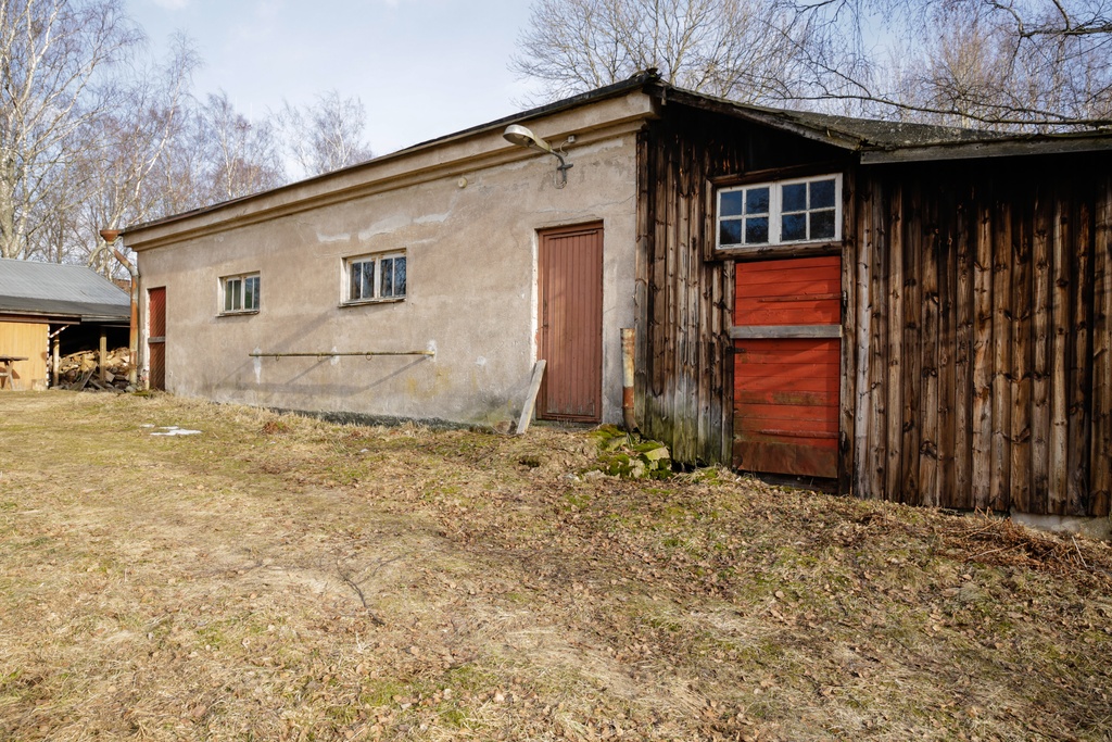 Paloaseman palokalustovaja Vallisaaressa. Siinä säilytettiin aikanaan T-mallista Fordia, kuorma-autoa ja hevosvetoisia kärryjä. Keskimmäisestä ovesta kuljettiin kahden hevosen talliin ja viereisestä punaisesta ovesta hevosten rehu- ja heinävarastoon. Pihapiiriin kuuluu myös vasemmassa reunassa näkyvä puusepänverstas. Valokuva on otettu aurinkoisella säällä.