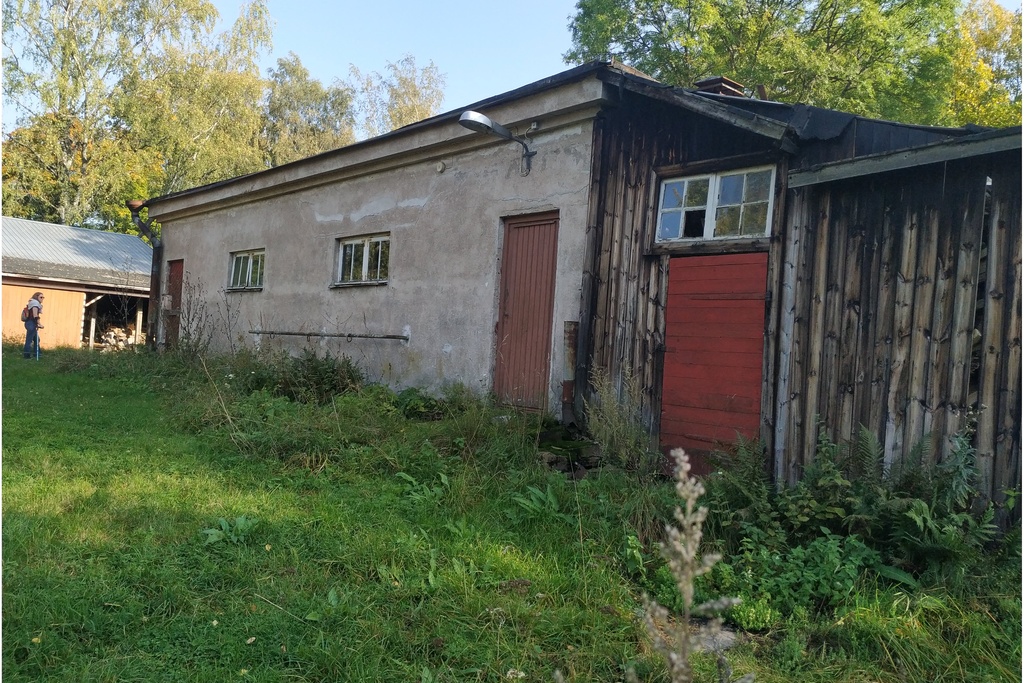 Paloaseman palokalustovaja Vallisaaressa. Siinä säilytettiin aikanaan T-mallista Fordia, kuorma-autoa ja hevosvetoisia kärryjä. Keskimmäisestä ovesta kuljettiin kahden hevosen talliin ja viereisestä punaisesta ovesta hevosten rehu- ja heinävarastoon. Pihapiiriin kuuluu myös vasemmassa reunassa näkyvä puusepänverstas. Valokuva on otettu aurinkoisella säällä. rephoto