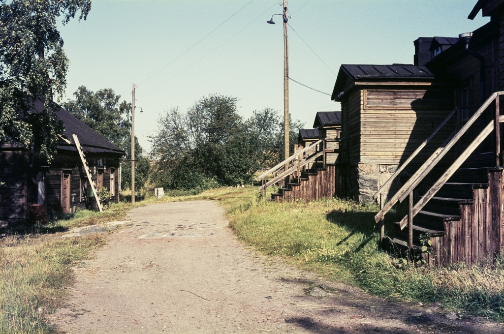Kylänraitti Vallisaaressa. Tien vasemmalla puolen on kauppa ja oikealla puolen vanhan kasarmin rakennus monine sisäänkäynteineen. Kauppa oli alunperin venäläisen varuskunnan keittiö ja kasarmi rakennettu 1860-luvulla niin ikään venäläiselle varuskunnalle. Kasarmissa toimi myöhemmin keskussääasema sekä 1950-luvun loppupuolelle asti koulu. Molemmat rakennukset purettiin 1960-luvun lopulla.
