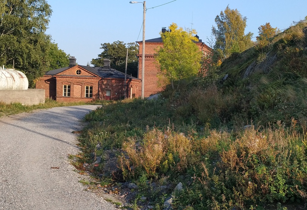 Näkymä Vallisaaresta. Oikealla on luotsitalo ja keskellä näkyy luotsitalon saunan ja pesutuvan rakennus. Vasemmalla alunperin venäläisten varuskuntansa saunaksi rakentama talo. Se on nykyään jo purettu. Tie rakennusten luo on säilynyt. rephoto