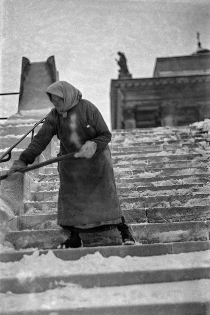 Nainen lunta lapioimassa Tuomiokirkon portailla.