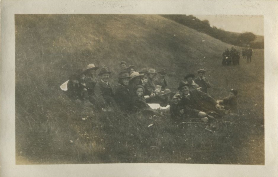 Group seated on a grassy bank with another group of people walking towards them