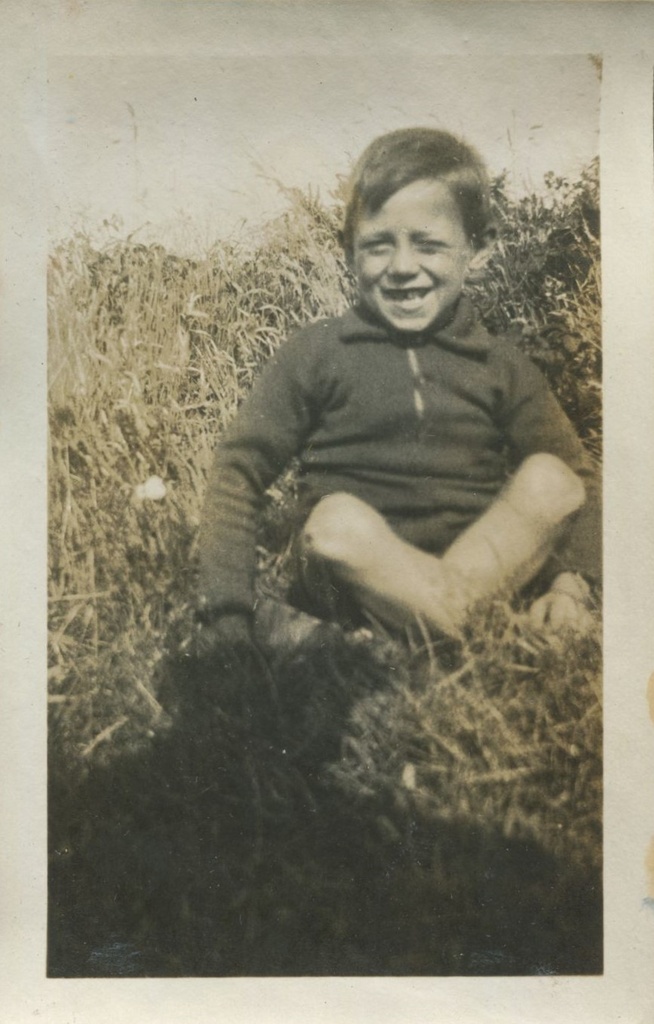 Young boy grinning, seated on the grass