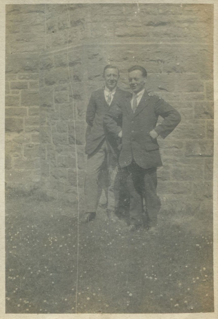 Two men standing in front of castle walls, one with hands on hips