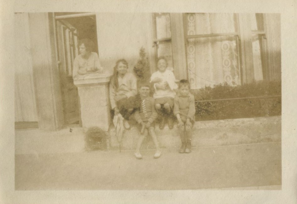 Children seated on the wall outside a house with one leaning on the post