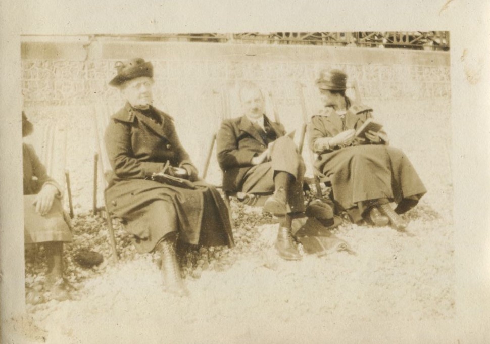 Two women and a man seated in deckchairs on the beach with books in hand