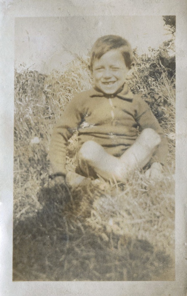 Young boy grinning, seated on the grass, Patcham, 1920