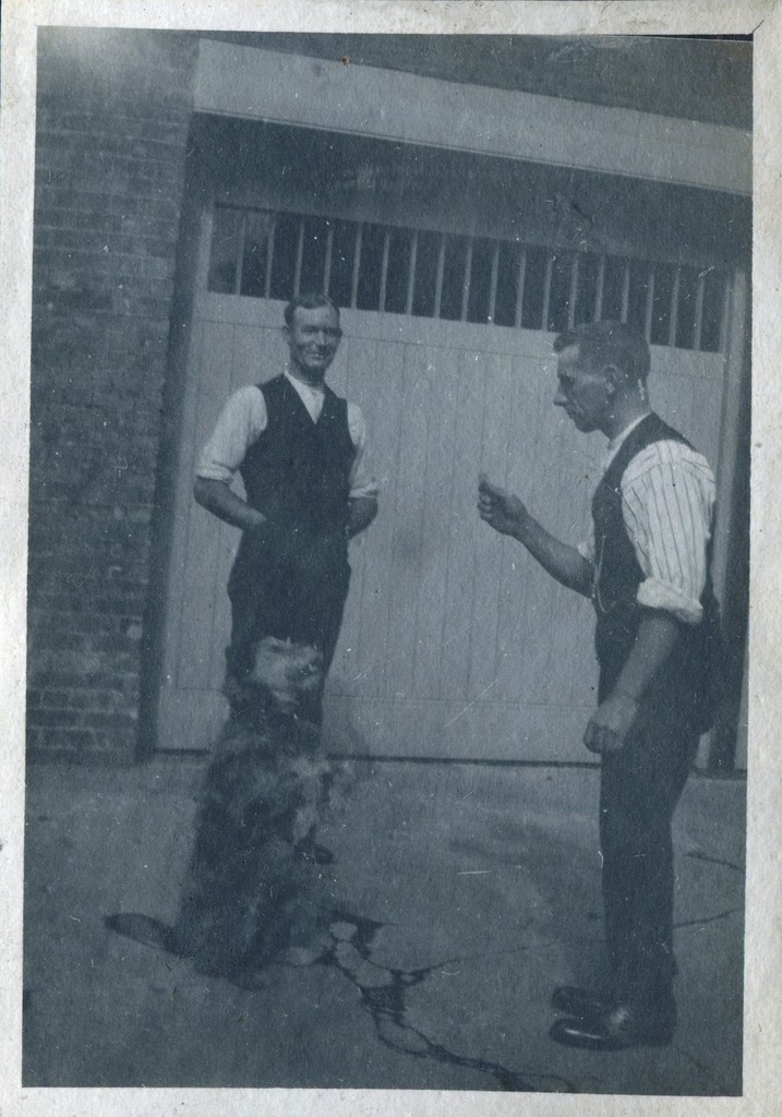 Man encouraging dog to beg for a treat, with another man standing behind. St Mary's Stables, Bedfont, Middlesex, 1920