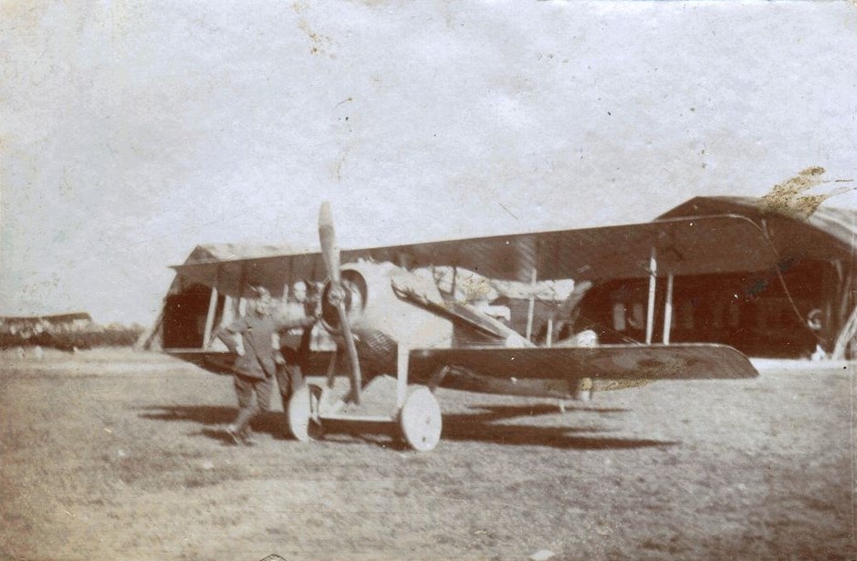 SPAD VII bi-plane with man standing by the propeller, in front of hanger