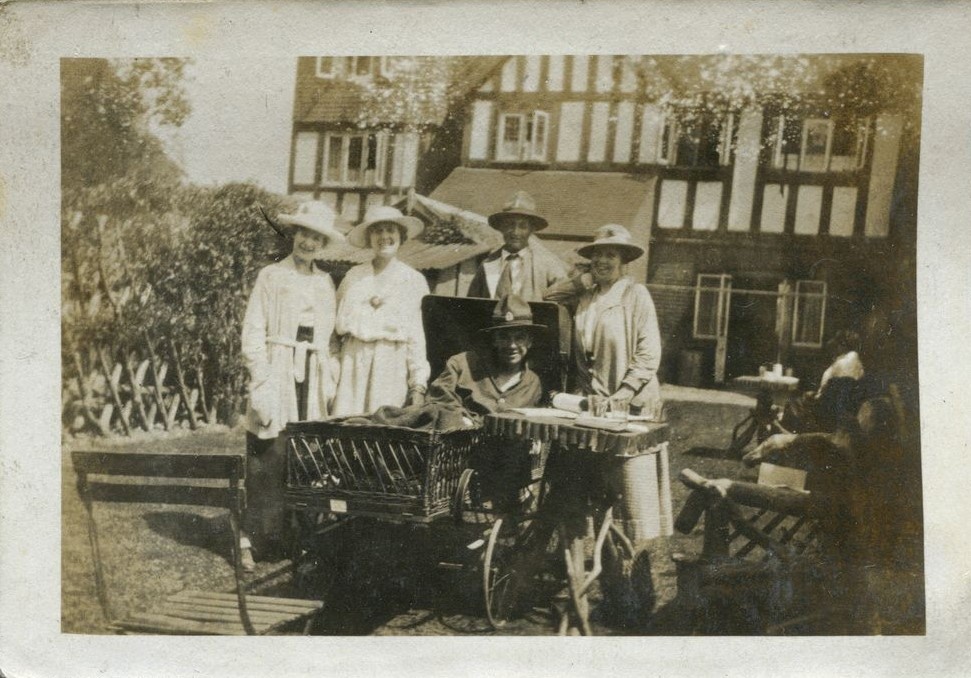 Man in a wheelchair surounded by another man and three ladies outside Ye olde Tea Shoppe, Brockenhurst 1918