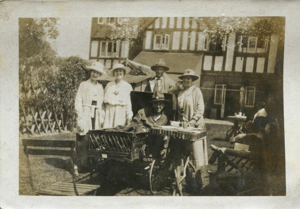 Man in a wheelchair surounded by another man and three ladies outside Ye olde Tea Shoppe, Brockenhurst 1918