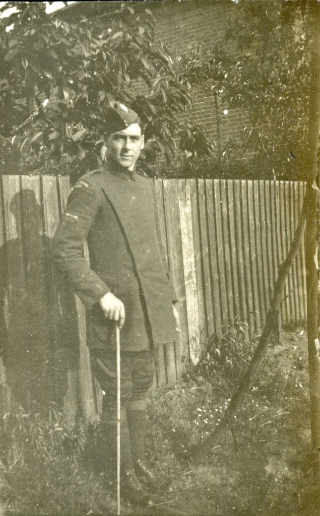 First World War soldier standing in front of a fence holding a walking stick