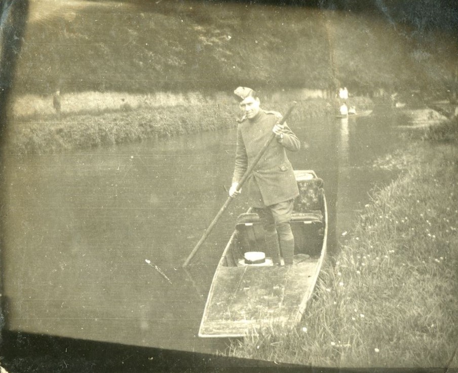 Man in First World War soldier's uniform, standing in a punt, smoking a pipe, with boater hat next to him