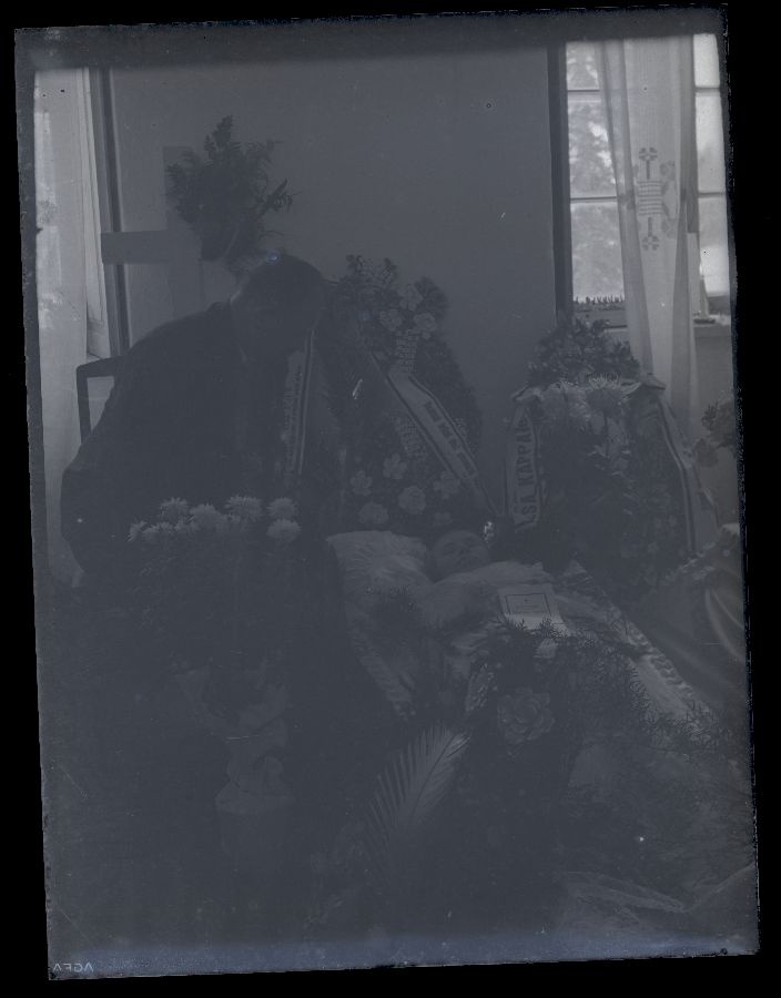 Matusefoto, naine avatud kirstus, kirstu kõrval istub meesterahvas.