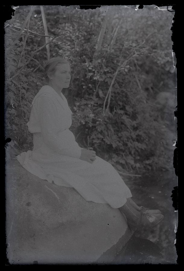 Valges kleidis naine istub jõe ääres kivil.