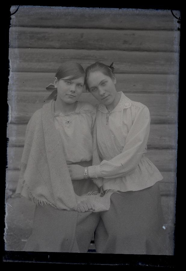 Kaks noort naist, poseerivad talumaja seina ees.