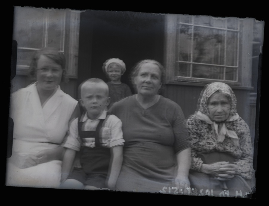 Kolm naist ja kaks väikest last maja ees.