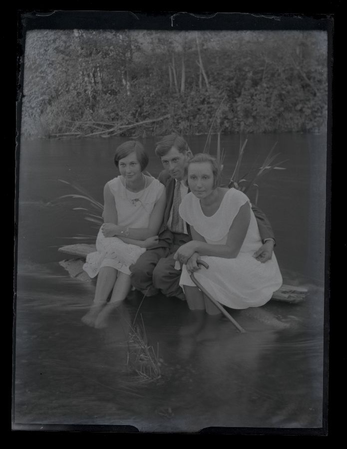 Kaks naist ja mees istuvad jões oleval kivil.