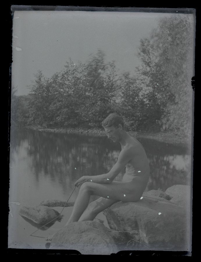 Alasti mees veekogu ääres kivil.