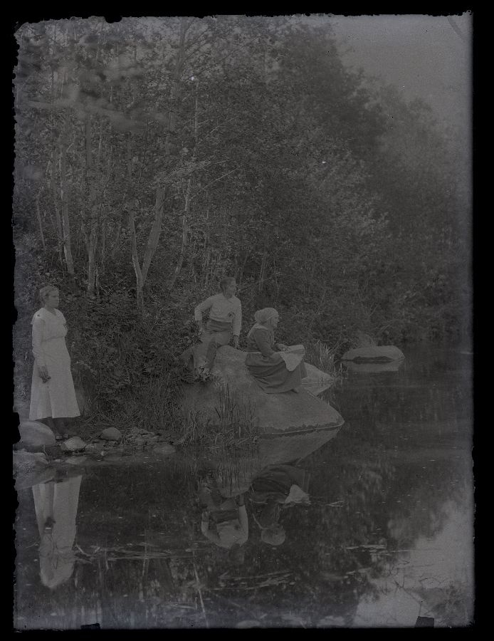 Vaade jõele ja jõekaldale, kaldal oleval kivil istuvad kaks naist, üks seisab kivi kõrval.