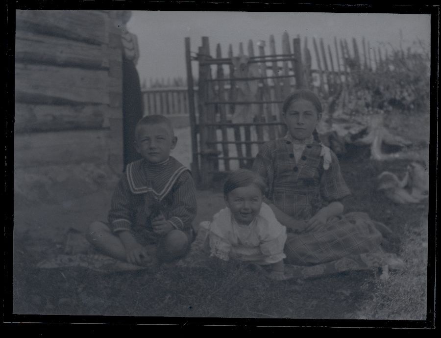 Kolm last murul, taustal näha majanurk ja aed.