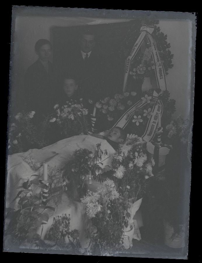 Matusefoto, väike laps avatud kirstus, kirstu taga seisavad kolm inimest.